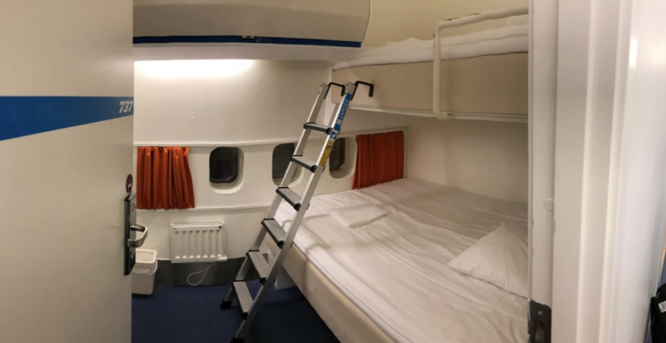 A compact cruise ship cabin with an upper and lower bunk bed and ladder