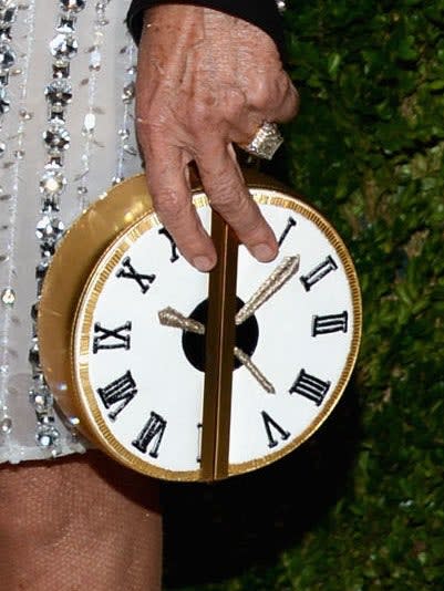 Person holding a unique clock-face styled clutch bag at an event