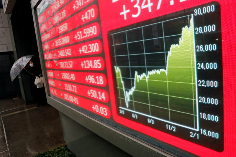 A woman holding umbrella walks near an electric board showing Nikkei index at a brokerage in Tokyo