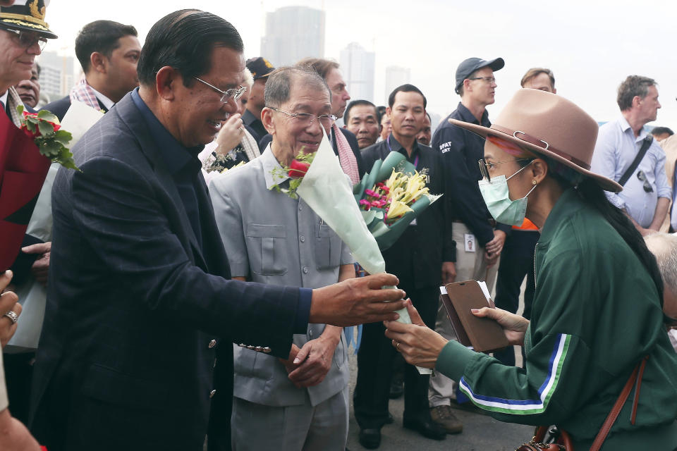 FILE - In this Feb. 14, 2020, file photo, Cambodia's Prime Minister Hun Sen, left, gives a bouquet of flowers to a passenger who disembarked from the MS Westerdam at the port of Sihanoukville, Cambodia. The feel-good story of how Cambodia allowed the cruise ship to dock after it was turned away elsewhere in Asia for fear of spreading the deadly virus that began in China has taken a dark turn after a passenger released from the ship tested positive for the virus. (AP Photo/Heng Sinith, File)