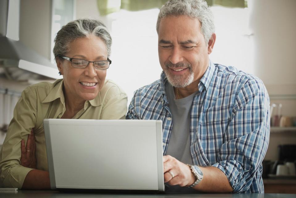 Two investors smile while looking at something on a laptop at home.