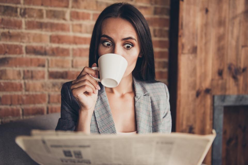 A person sips a coffee while looking at a newspaper.