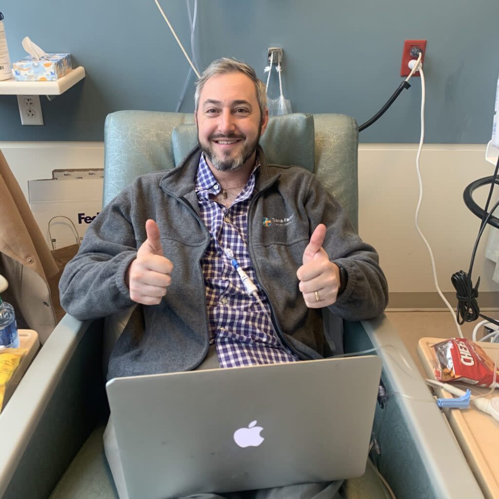 A man in a hospital recliner holding his thumbs up while receiving chemotherapy treatment.