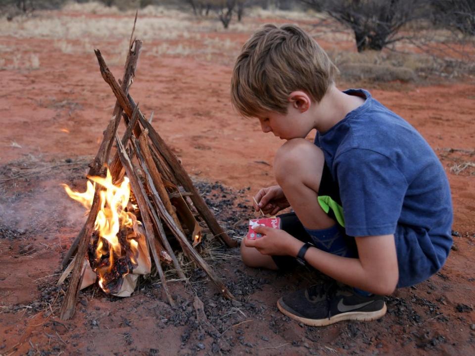 A boy tending to a camp fire while camping.