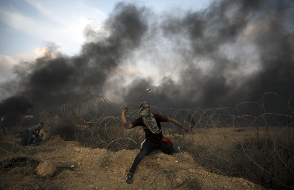 A Palestinian protester hurls stones towards Israeli troops at the Gaza Strip's border with Israel, Friday, Oct. 19, 2018. (AP Photo/Khalil Hamra)