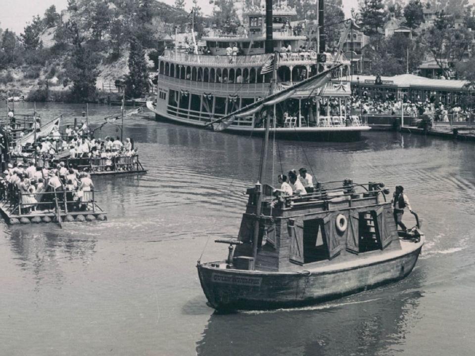 Black and white photo of a wooden tall boat in a river with other boats and rafts.