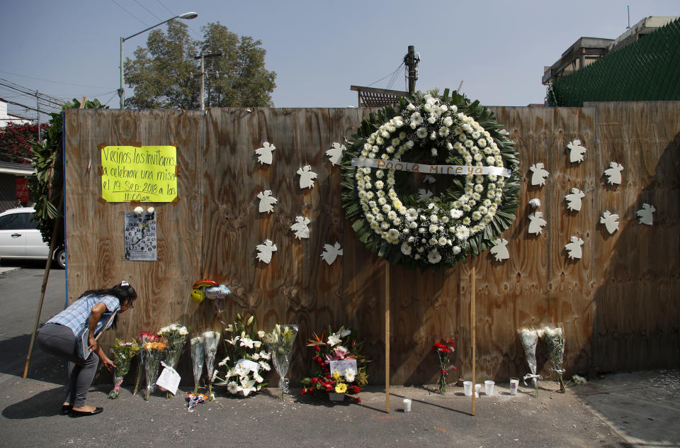 A woman places a floral bouquet on the perimeter wall of the collapsed Enrique Rebsamen elementary school in Mexico City, Sept. 19, 2018. The school collapsed one year ago killing scores of children in the 7.1 earthquake that struck the city. Officials said the owner of the private school built an apartment for herself on top of the school wing that collapsed, which may have played a role in the tragedy. (AP Photo/Eduardo Verdugo)