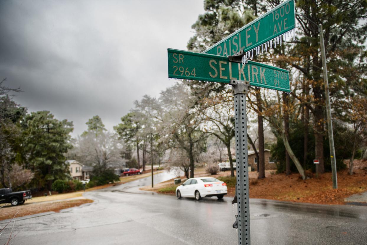 Ice covers a street sign as a car drives slowly down Paisley Avenue in Fayetteville on Sunday, Jan. 16, 2022.