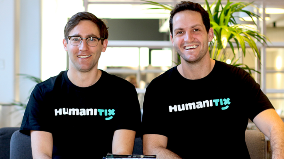 Adam McCurdie and Josh Ross from Humanitix are wearing black and white t-shirts and smiling at the camera.