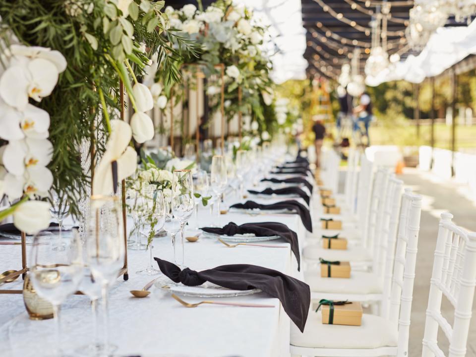 Table at wedding with white table cloths, greenery, and black napkins