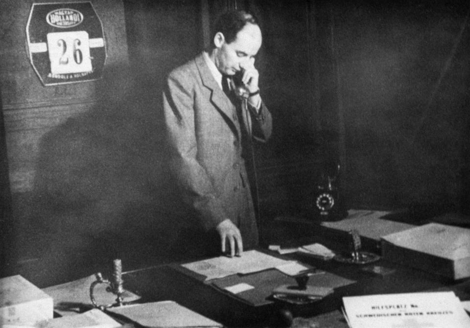 raoul wallenberg holds a phone to his ear and looks down at papers on a desk