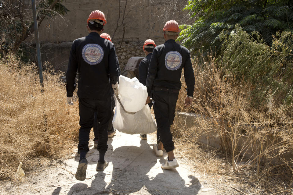 In this Saturday, Sept. 7, 2019 photo, first responders remove a body at the site of a mass grave in Raqqa, Syria. First responders said they have pulled nearly 20 bodies out of the latest mass grave uncovered in Raqqa, the Syrian city that was the de facto capital of the Islamic State group. It is the 16th mass grave in the city, and officials are struggling with a lack of resources needed to document and one day identify the thousands of dead who have been dug out. (AP Photo/Maya Alleruzzo)