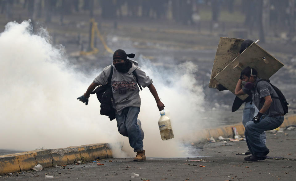 An anti-government protester carries a container of water, with an active tear gas canister inside, after the canister was fired by police during a military curfew near the National Assembly in Quito, Ecuador, Sunday, Oct. 13, 2019. Deadly protests against a plan to remove fuel subsidies as part of an International Monetary Fund austerity package have gone on for more than a week. (AP Photo/Dolores Ochoa)