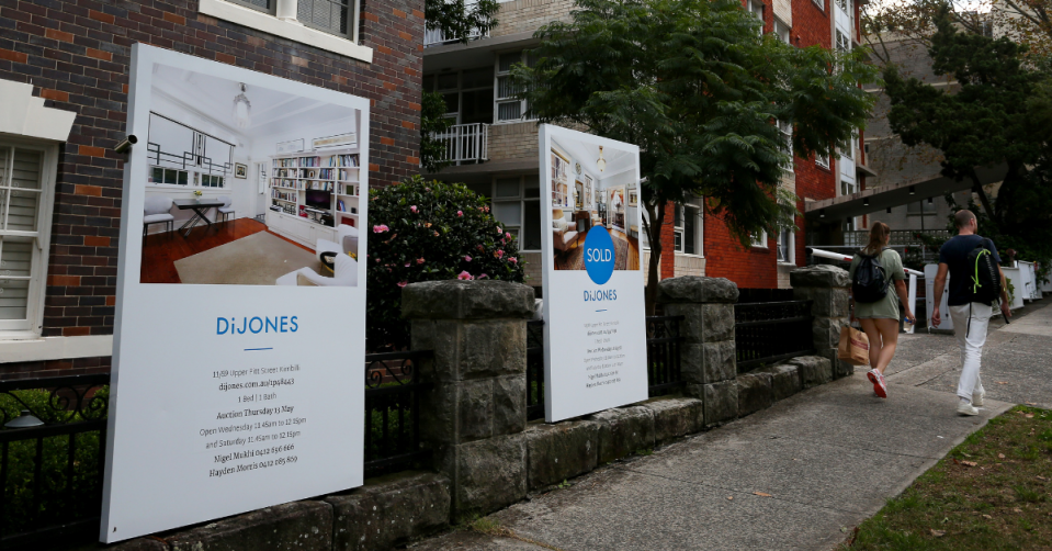 Street view of units for two for sale signs out the from, one with a sold sticker, and people walking past.