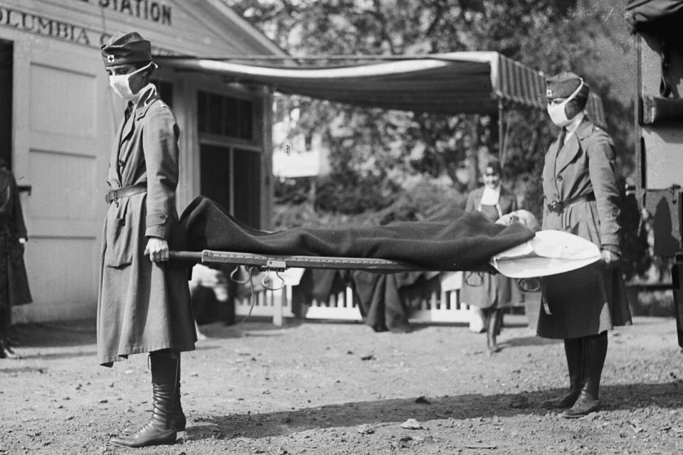 Black and white photo of two people wearing masks holding someone on a stretcher