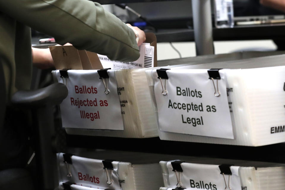 A Miami-Dade County Elections Department employee places a vote-by-mail ballot for the August 18 primary election into a box for rejected ballots as the canvassing board meets at the Miami-Dade County Elections Department, Thursday, July 30, 2020, in Doral, Fla. President Donald Trump is for the first time publicly floating a "delay" to the Nov. 3 presidential election, as he makes unsubstantiated allegations that increased mail-in voting will result in fraud. (AP Photo/Lynne Sladky)