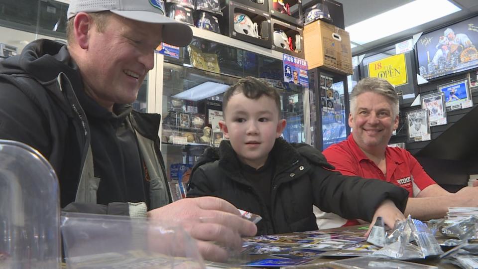 Fiver-year-old Barry Geluch with his father Joe, left, and Langley-based hobby shop owner Ken Richardson. The father-son duo grabbed a rare Connor Bedard printing plate, once used to manufacture the cards found in the Upper Deck collection series.  (CBC News - image credit)