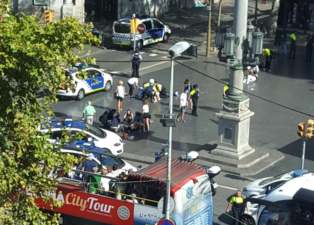 Injured are helped by responders as a tour bus passes by after a white van jumped the sidewalk in the historic Las Ramblas district of Barcelona, Spain, crashing into a summer crowd of residents and tourists Thursday, Aug. 17, 2017. According to witnesses the white van swerved from side to side as it drove into tourists and residents. (Daniel Vil via AP)