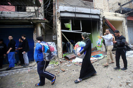 People carry belongings as they walk past damaged shops inside the Ain el-Hilweh refugee camp near Sidon, southern Lebanon, April 13, 2017. REUTERS/Ali Hashisho