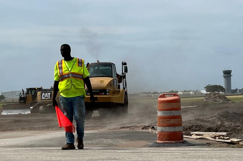 A construction worker prepares to flag traffic to halt to let construction vehicles cross the Bellevue Avenue Extension at Daytona Beach International Airport on Friday, May 10, 2024. The airport is clearing 54 acres along the north side of the road, south of the control tower, for future aviation/airline-related commercial development, thanks to a $5 million grant from the U.S. Economic Development Administration.