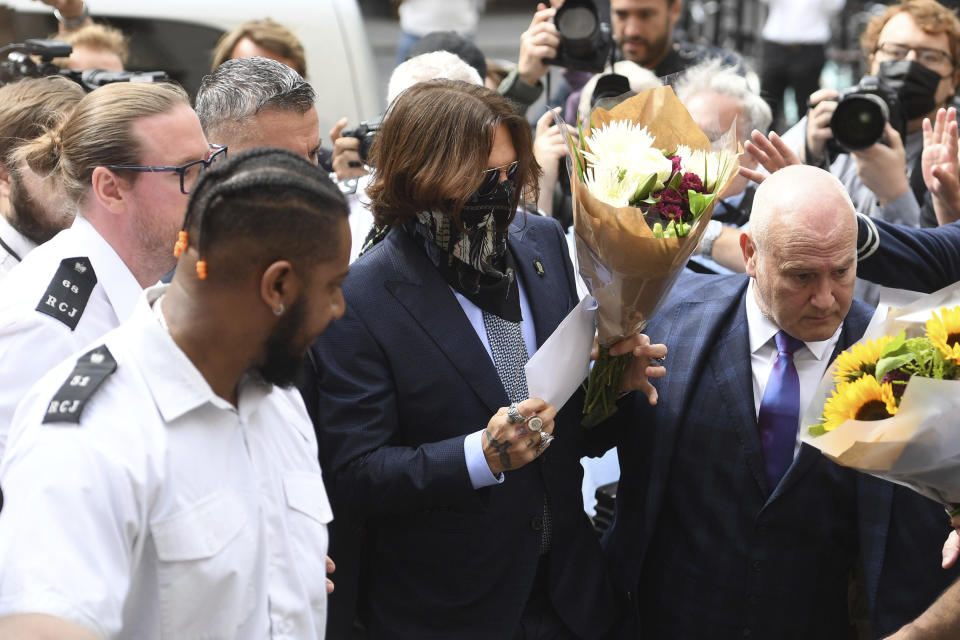 Actor Johnny Depp, centre, receives flowers as he arrives at the High Court for a hearing in his libel case, in London, Friday, July 24, 2020. Depp is suing News Group Newspapers, publisher of The Sun, and the paper's executive editor, Dan Wootton, over an April 2018 article that called him a "wife-beater." The Sun's defense relies on a total of 14 allegations by his ex-wife, actress Amber Heard of Depp's violence. He strongly denies all of them. (Kirsty O'Connor/PA via AP)