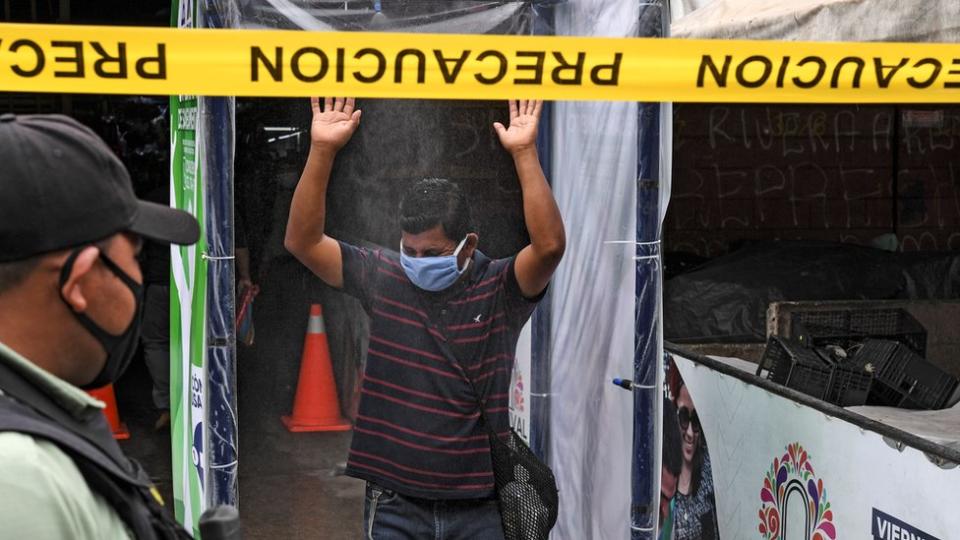 Un policía vigila gente en una cabina sanitaria de El Salvador.