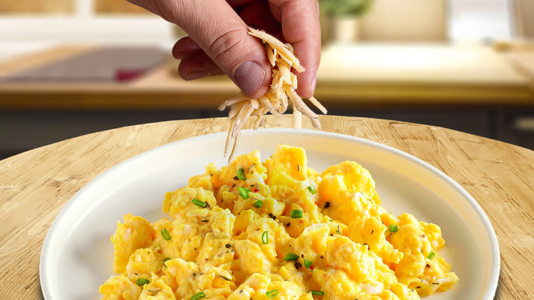 Fingers putting cheese on scrambled eggs