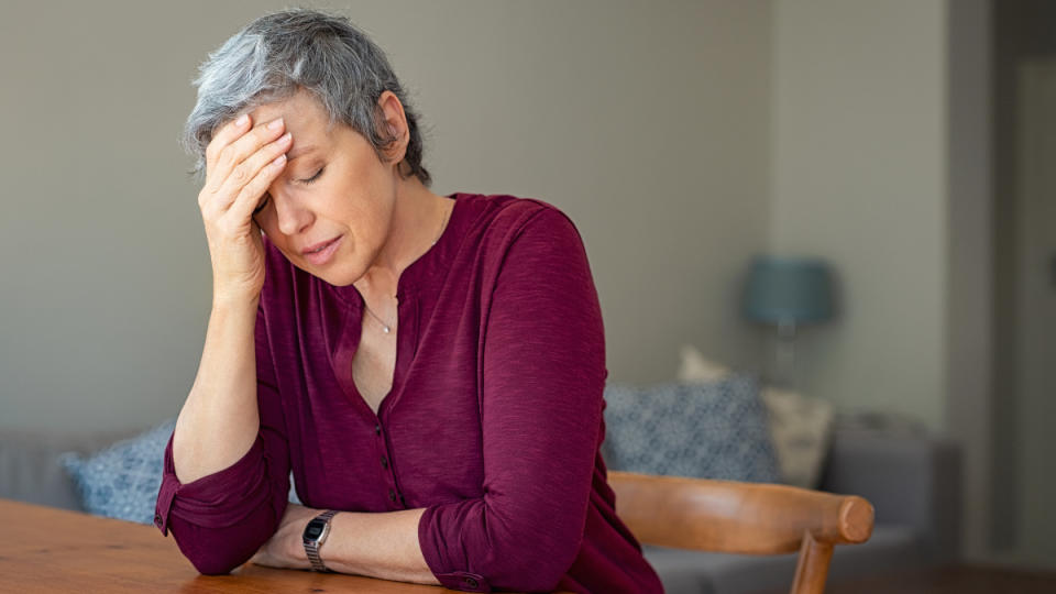 A woman with short grey hair and plum-colored top with her her in hand resting on a table, exhausted from a weak vagus nerve