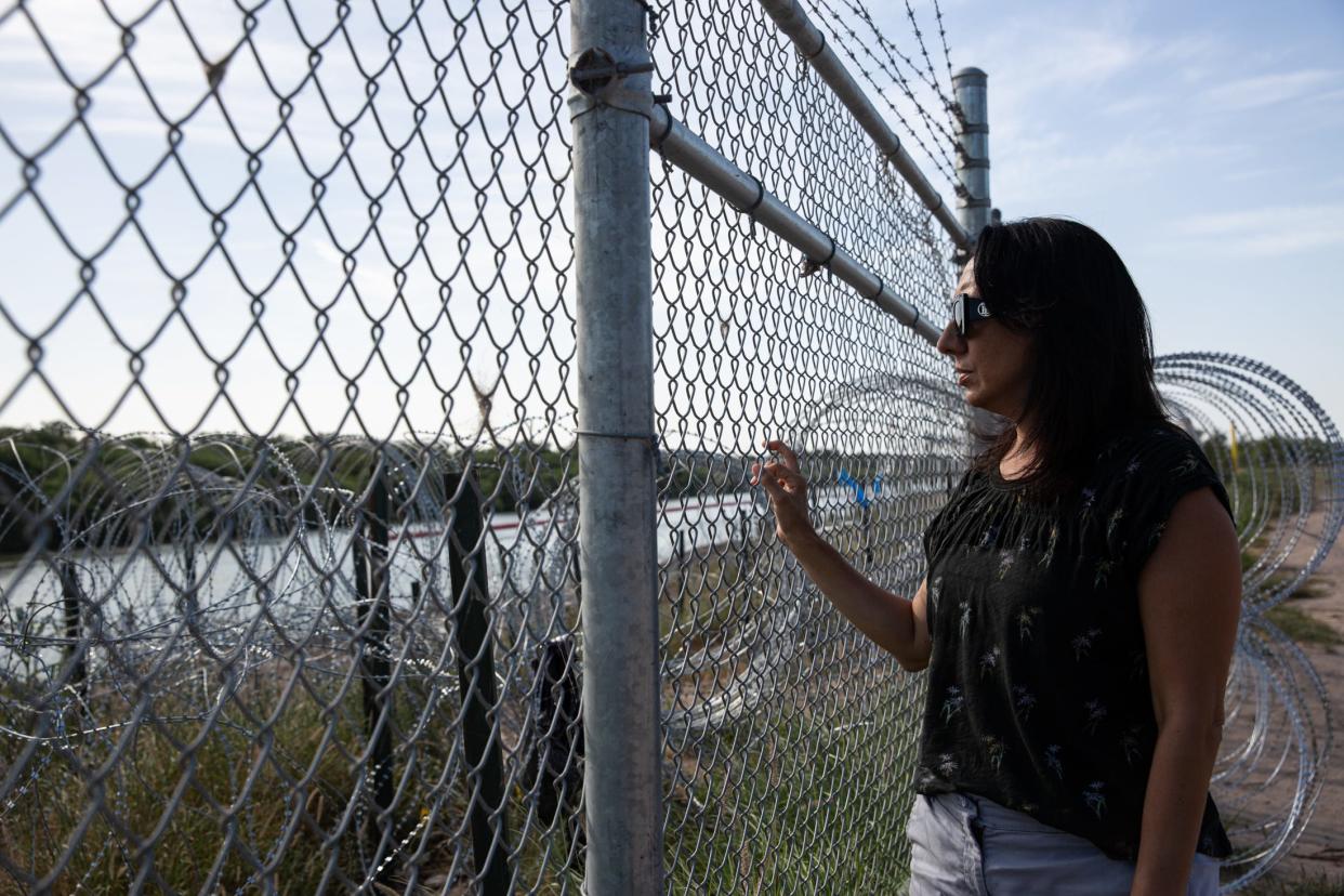 Magali Urbina, 52, owner of pecan orchard Heavenly Farms, looks through a chain link fence and razor wire cutting through her property at the Rio Grande on July 20 in Eagle Pass, Texas.