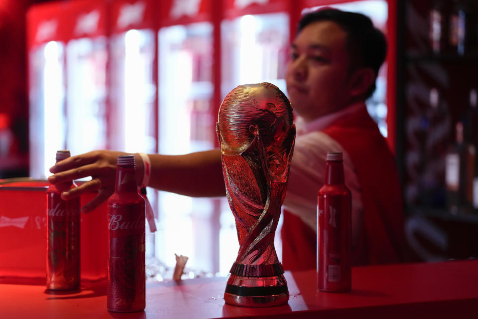 A bartender clears bottles of Budweiser beer from the bar near a replica of the FIFA World Cup trophy at an official U.S. Soccer fan party at the Budweiser World Club, in Doha, Sunday, Nov. 20, 2022. (AP Photo/Ashley Landis)