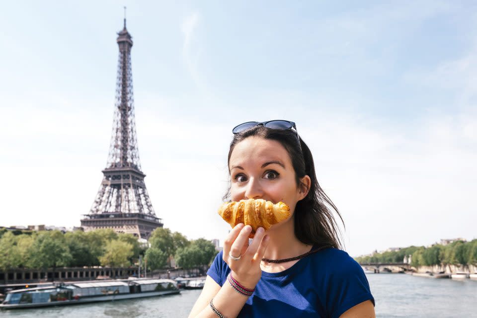 a woman standing with a croissant near her face with the eiffel tower at the back
