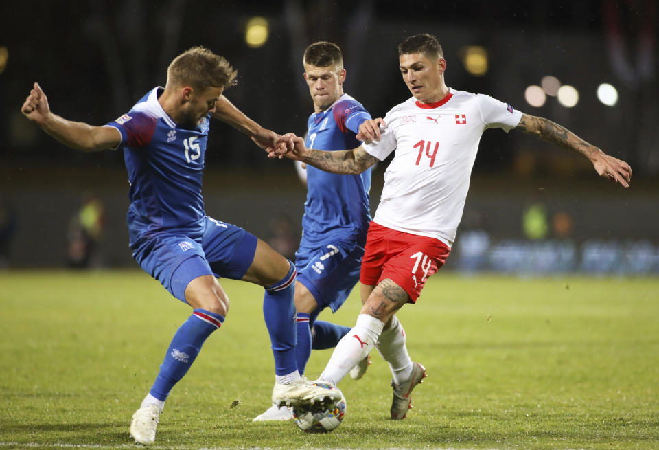 Switzerland's Steven Zuber (14), right, is challenged by Iceland's Holmar Eyjolfsson (15), left, and Johann Gudmundsson (7), centre, during the UEFA Nations League soccer match between Iceland and Switzerland at Laugardalsvollur stadium in Reykjavik, Iceland, Monday Oct. 15, 2018. (AP Photo/Brynjar Gunnarsson)