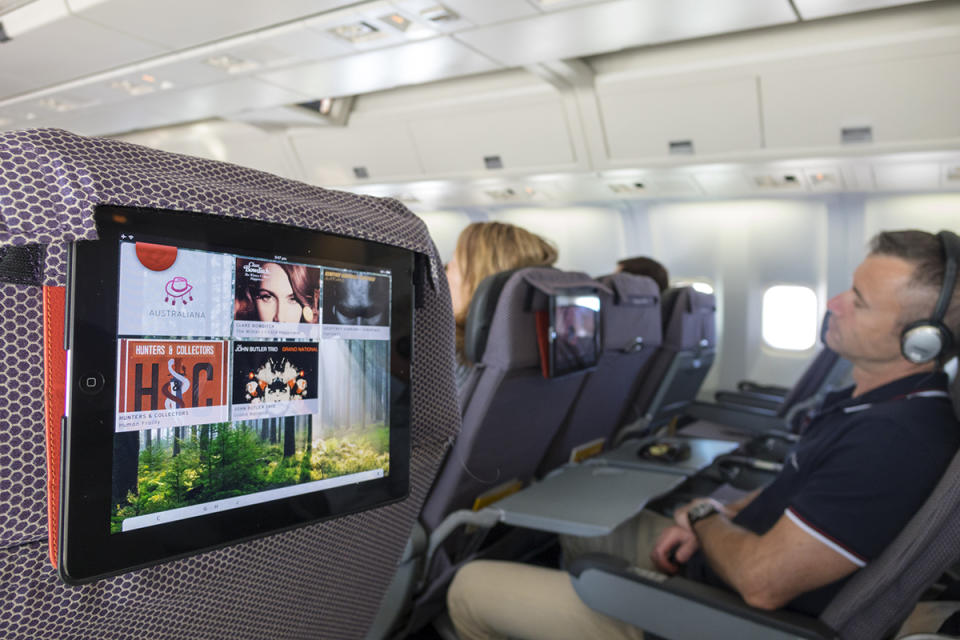 Inside Qantas aeroplane, entertainment screen and male passenger with headphones on