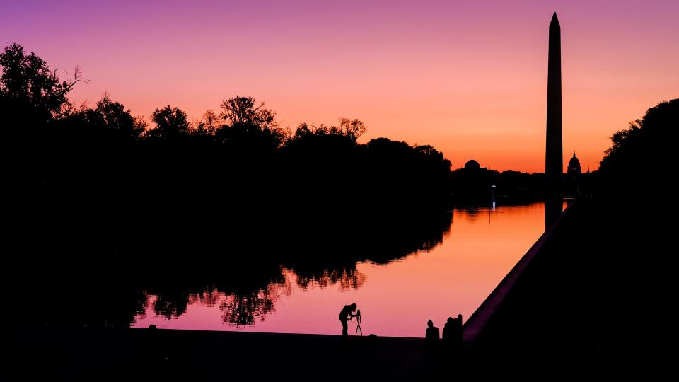 In this Sept. 21, 2019, file photo, a photographer lines up her shot at the National Mall reflecting pool as the sun begins to rise behind the Washington Monument and the U.S. Capitol building in Washington.
