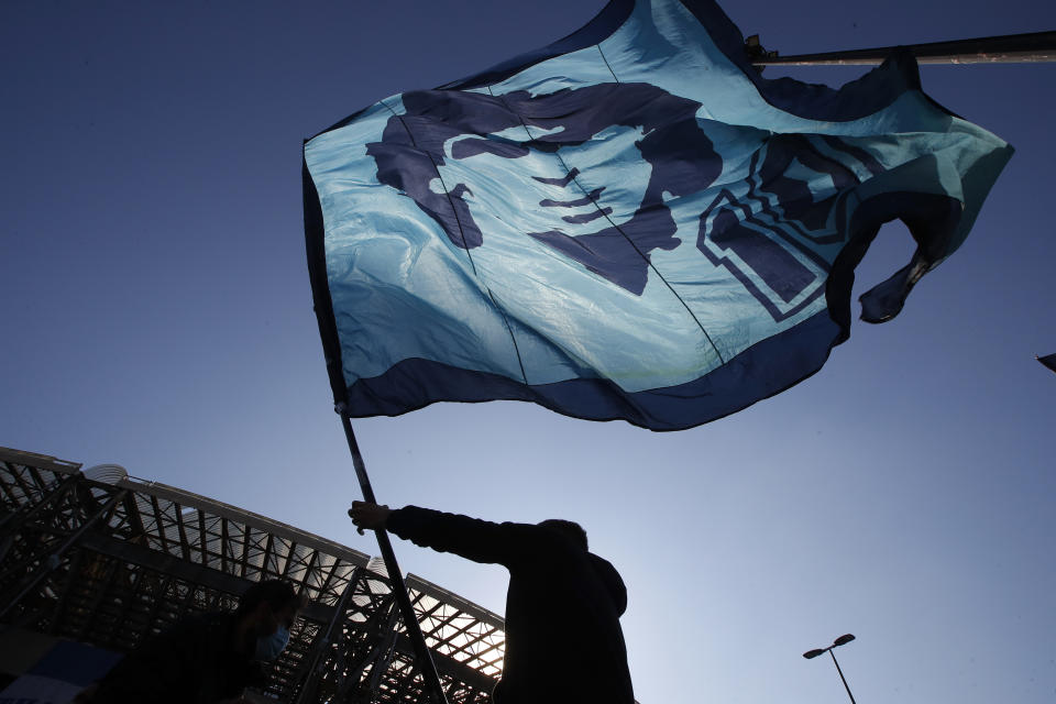 A man waves a flag commemorating soccer legend Diego Maradona outside the San Paolo stadium, in Naples, southern Italy, Thursday, Nov. 26, 2020. Maradona died Wednesday, Nov. 25, 2020 in Buenos Aires. (AP Photo/Alessandra Tarantino)