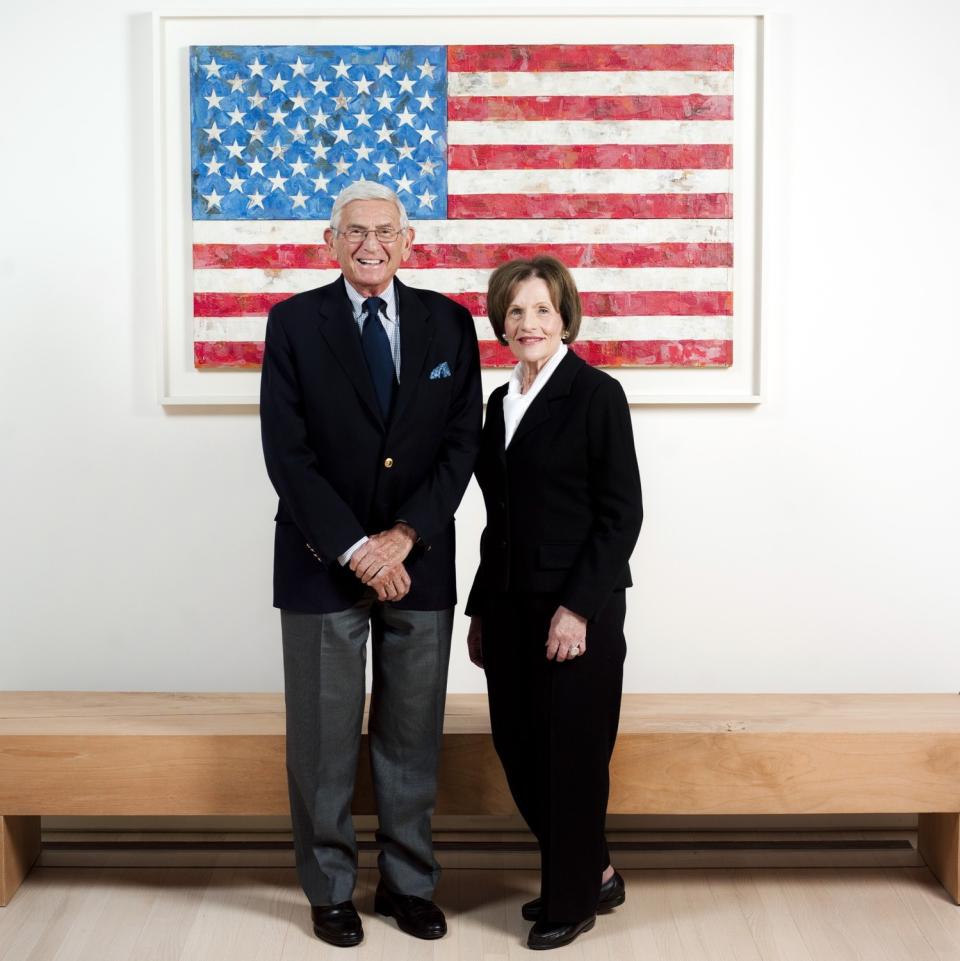PEli and Edythe Broad stand in front of a Jasper Johns painting of the American flag.