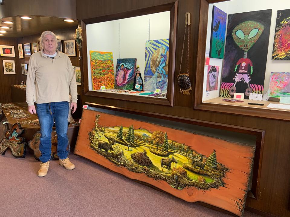 William Caouette, who owns the Dot Line Curve Creations Gift Gallery with his wife, Paula Abare, stands in his shop at 33 Parker St. in Gardner. The large wood carving at his feet is the work of Winchendon artist Elie Bastarache.