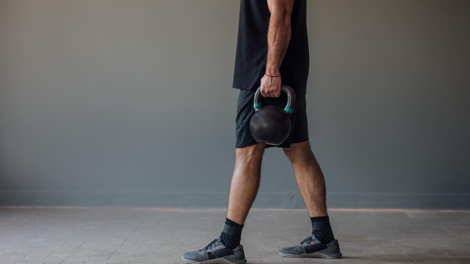 Man walking holding two kettlebells in farmer's walk