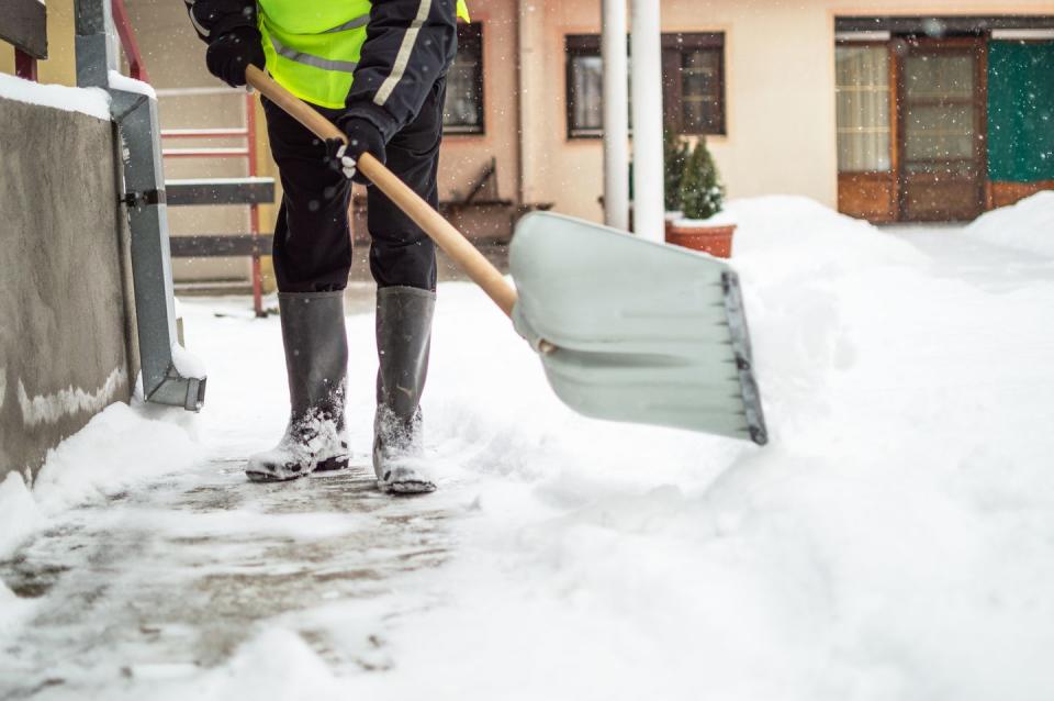 man with snow shovel cleans sidewalk