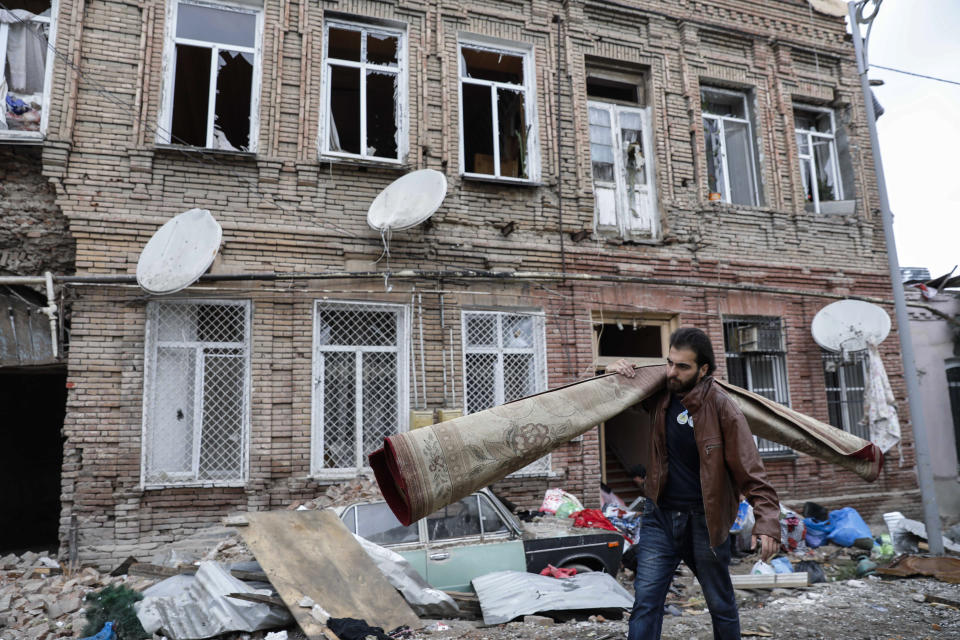 A person carries a carpet as he walks past buildings in a residential area in Ganja, Azerbaijan, damaged by shelling by Armenian forces, Monday, Oct. 5, 2020. The fighting between Armenian and Azerbaijani forces over the separatist territory of Nagorno-Karabakh resumed Monday, with both sides accusing each other of launching attacks. The region lies in Azerbaijan but has been under the control of ethnic Armenian forces backed by Armenia since the end of a separatist war in 1994. (Unal Cam/DHA via AP)