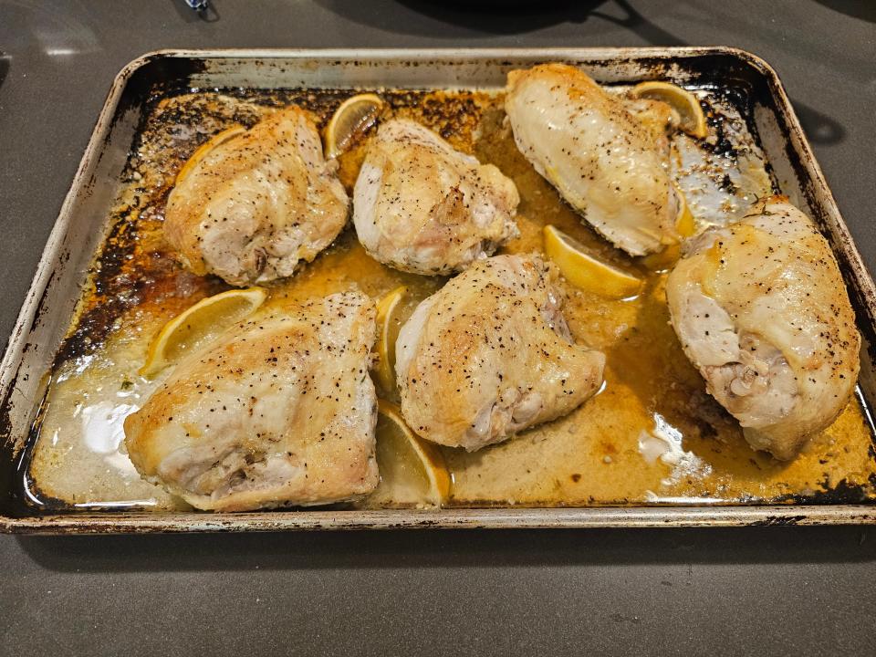 Cooking sheet of cooked pieces of chicken with juices and lemon wedges