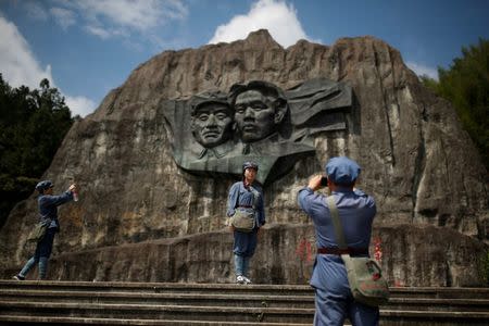 Participants dressed in replica red army uniforms take pictures at a base relief showing former Chinese communist leaders Mao Zedong and Zhu De at a historic site of the Long March in the mountains outside Jinggangshan, Jiangxi province, China, September 14, 2017. REUTERS/Thomas Peter
