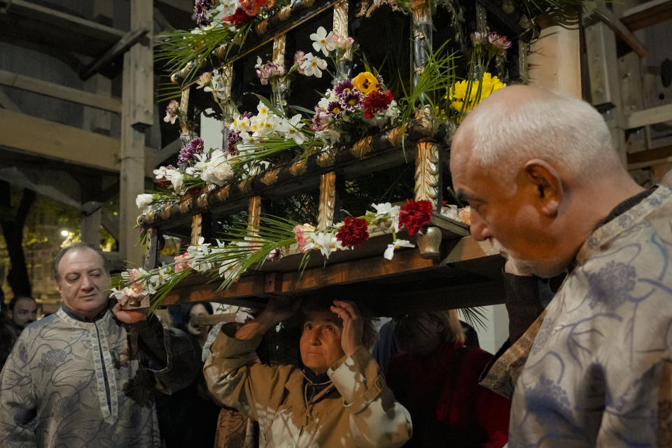 A woman stops to touch a wooden structure depicting the coffin of Jesus Christ as she passes underneath it during the Good Friday funeral procession at the Armenian Cathedral in Bucharest, Romania, Friday, April 14, 2023. (AP Photo/Andreea Alexandru)