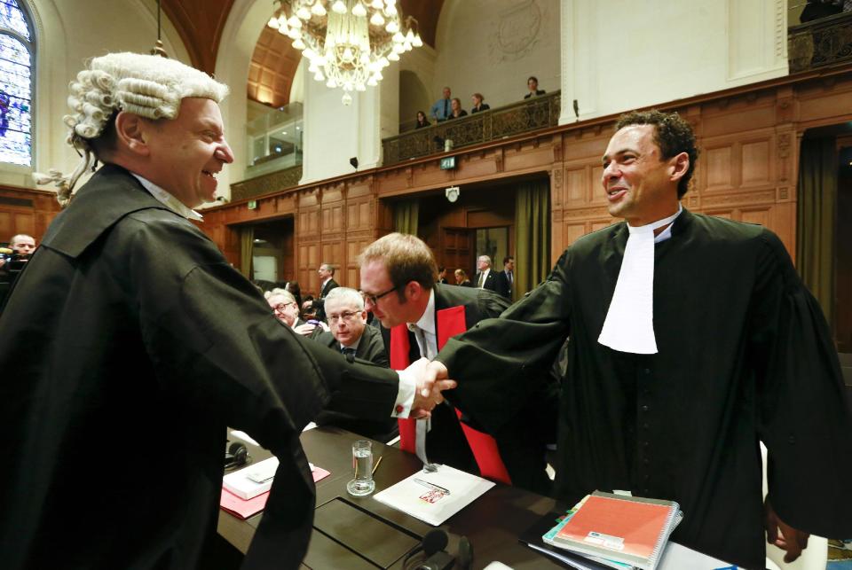 Counsel Philippe Sands of Croatia, left, shakes hands with Wayne Jordash of the Serbia delegation, right, prior to the start of public hearings at the International Court of Justice (ICJ) in The Hague, Netherlands, Monday, March 3, 2014. Croatia is accusing Serbia of genocide during fighting in the early 1990's as the former Yugoslavia shattered in spasms of ethnic violence, in a case at the United Nations' highest court that highlights lingering animosity in the region. Croatia is asking the ICJ to declare that Serbia breached the 1948 Genocide Convention when forces from the former Federal Republic of Yugoslavia attempted to drive Croats out of large swaths of the country after Zagreb declared independence in 1991. (AP Photo/Jiri Buller)