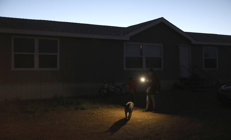 In this Wednesday, May 8, 2019 photo, Jimmy Long Jr. uses his cell phone flashlight to find his way to get something from his truck outside his Kaibeto home on the Navajo Reservation. Long has lived with his family in a home that had no electricity for more than a decade. An ambitious project to connect homes to the electric grid on the country's largest American Indian reservation is wrapping up. Utility crews from across the U.S. have volunteered their time over the past few weeks to hook up about 300 homes on the Navajo Nation. (AP Photo/Jake Bacon)