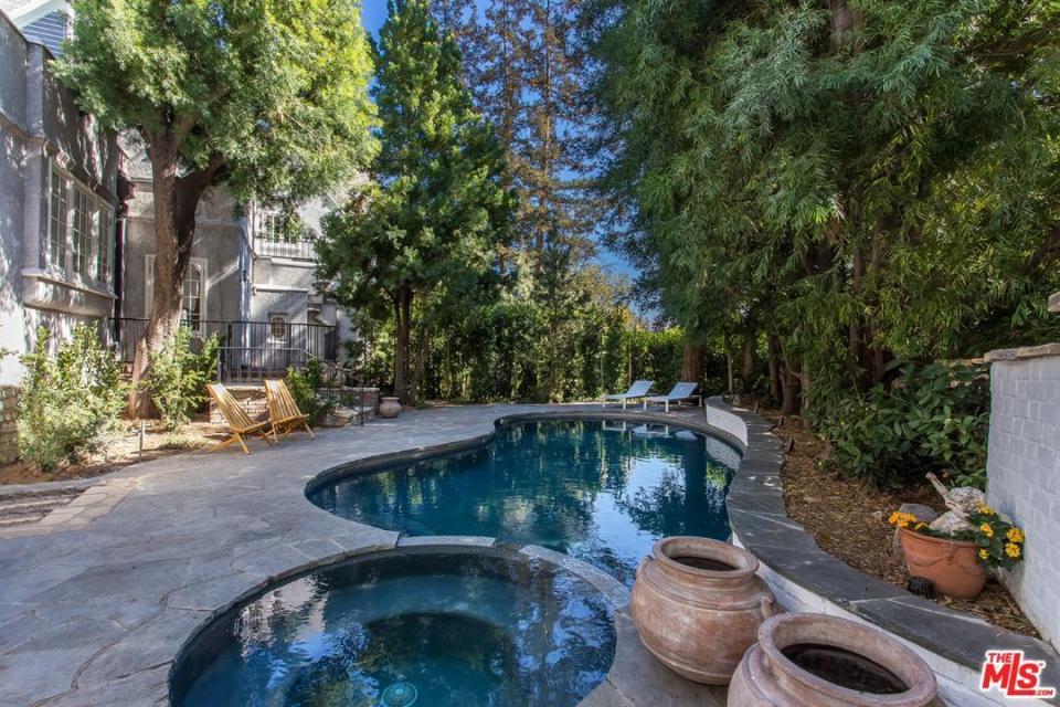 <p>A flagstone-surrounded swimming pool and spa, overlooked by mature trees in the grounds. (Redfin/MLS) </p>