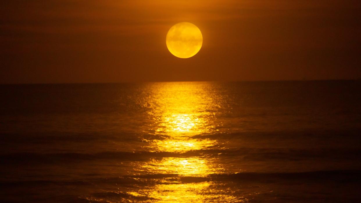  A bright full moon rises over the ocean, reflecting across the surface of the water. 