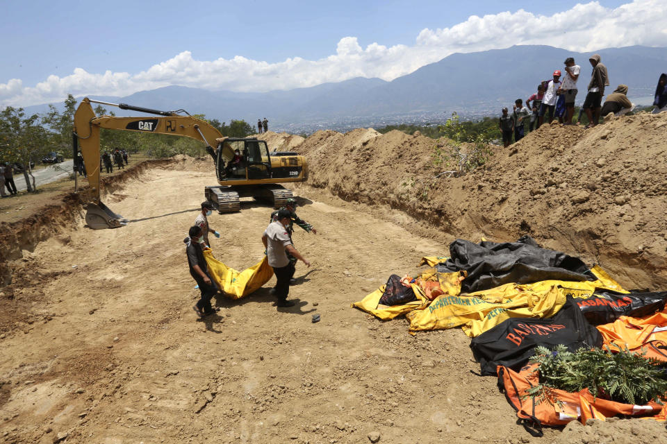 Indonesian police carry the body of a tsunami victim during a mass burial in Palu, Central Sulawesi, Indonesia, Monday, Oct. 1, 2018. A mass burial of earthquake and tsunami victims was being prepared in a hard-hit city Monday as the need for heavy equipment to dig for survivors of the disaster that struck a central Indonesian island three days ago grows desperate.(AP Photo/Tatan Syuflana)