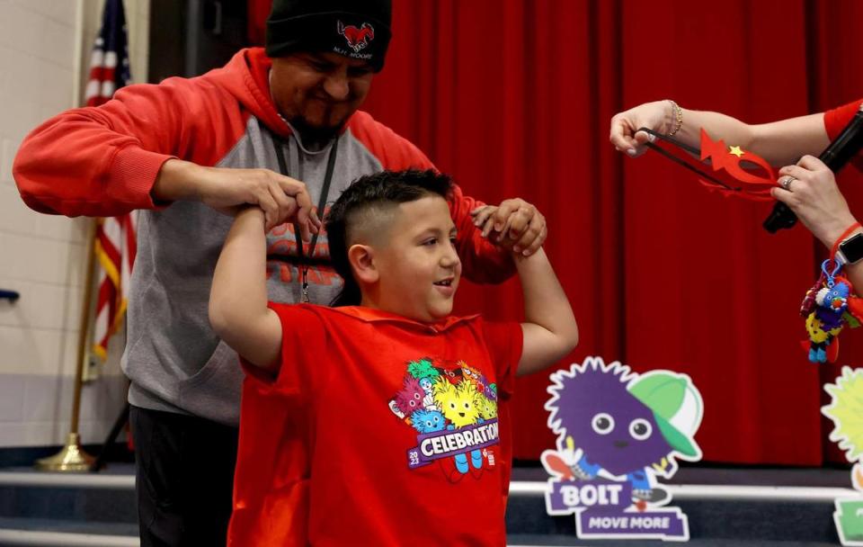 Ramon Rodriguez Jr., a second-grader at Cesar Chavez Elementary, puts on a cape and mask with the help of his former PE teacher Jose Ramirez during a school assembly on Friday, January 12, 2024. Rodriguez was named as a Youth Heart Ambassador for the American Heart Association.