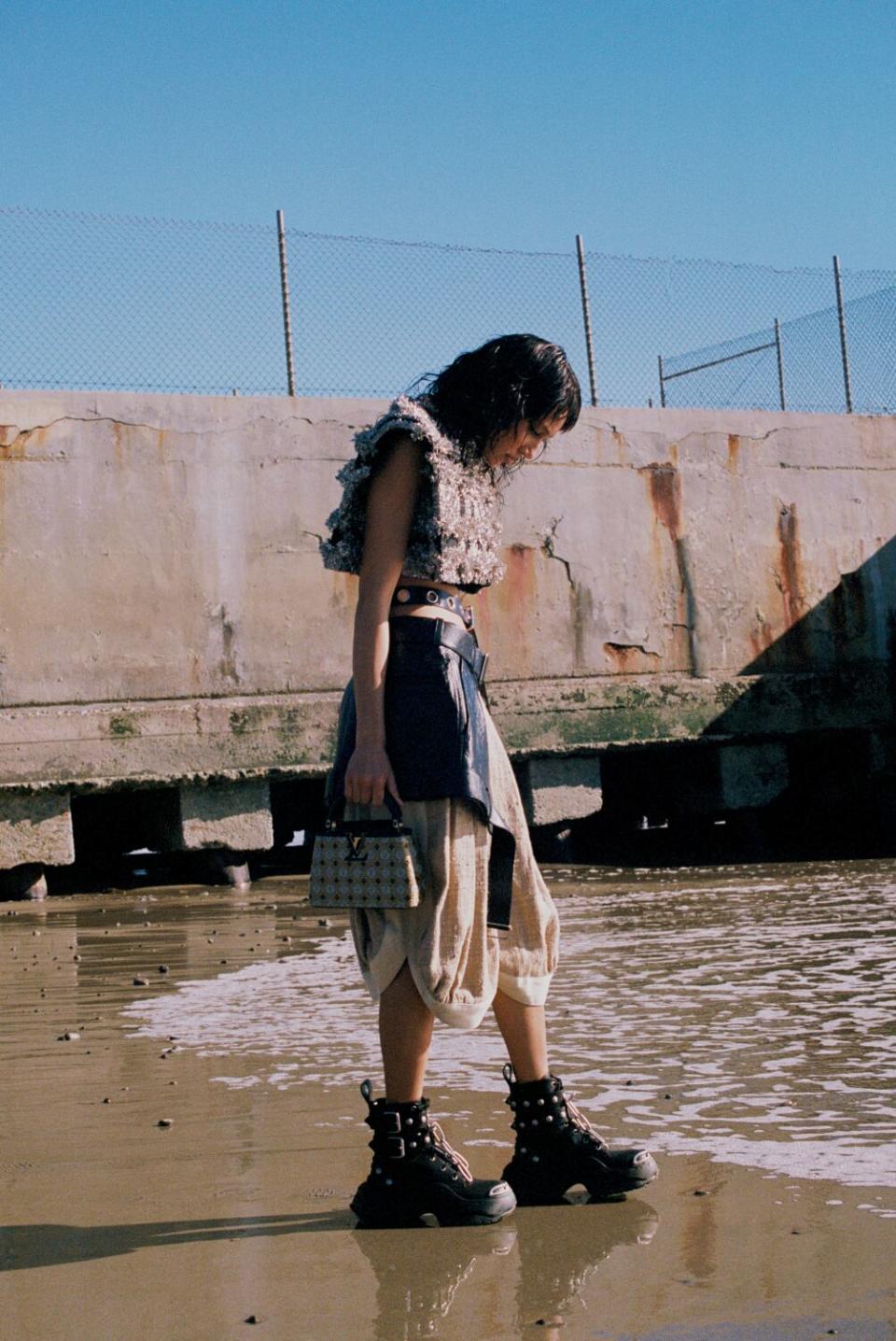 A woman wearing loose-fitting layers stands at a shore.